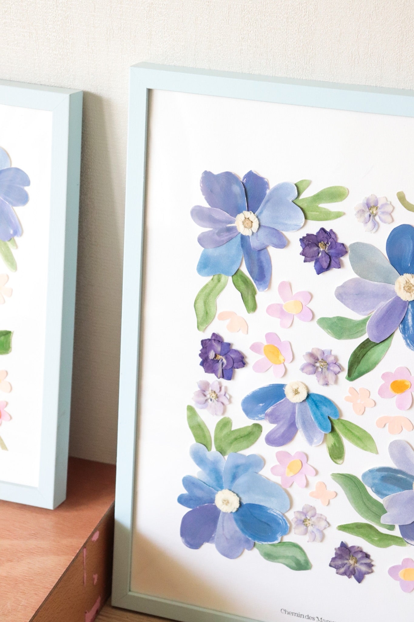 Grand herbier original A3 nommé Azuria, collage de fleurs en papier en relief sur fond blanc, encadré dans un cadre en bois bleu, création Chemin des Marettes.