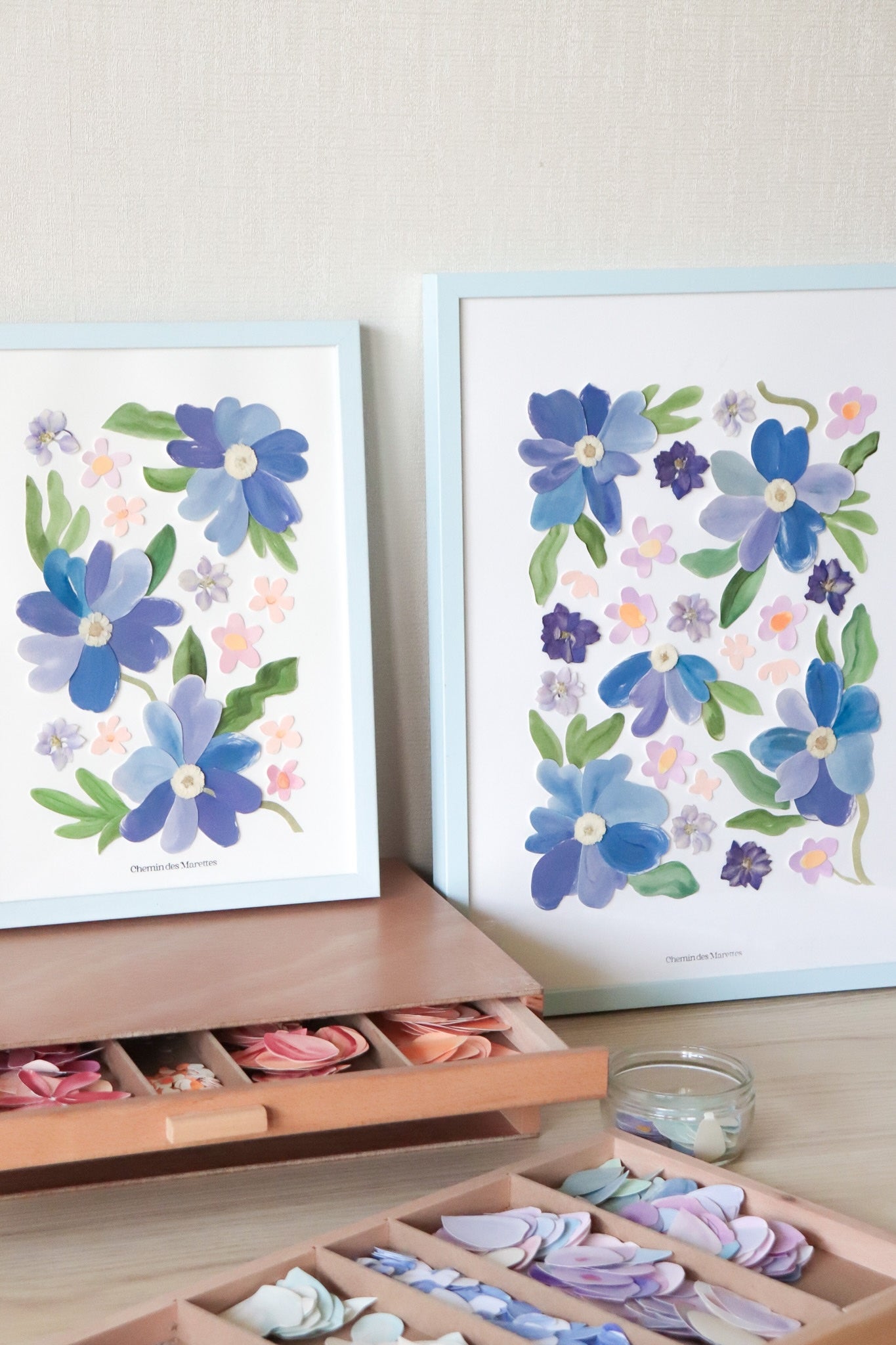 Grand herbier original A3 nommé Azuria, collage de fleurs en papier en relief sur fond blanc, encadré dans un cadre en bois bleu, création Chemin des Marettes.